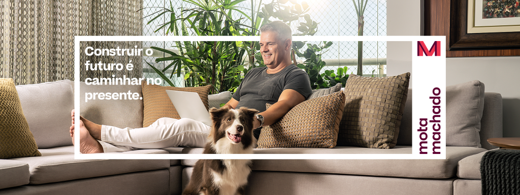 Foto de um homem sorridente sentado no sofá ao lado do seu cachorro. Uma das fotos oficiais da nova marca da Mota Machado.